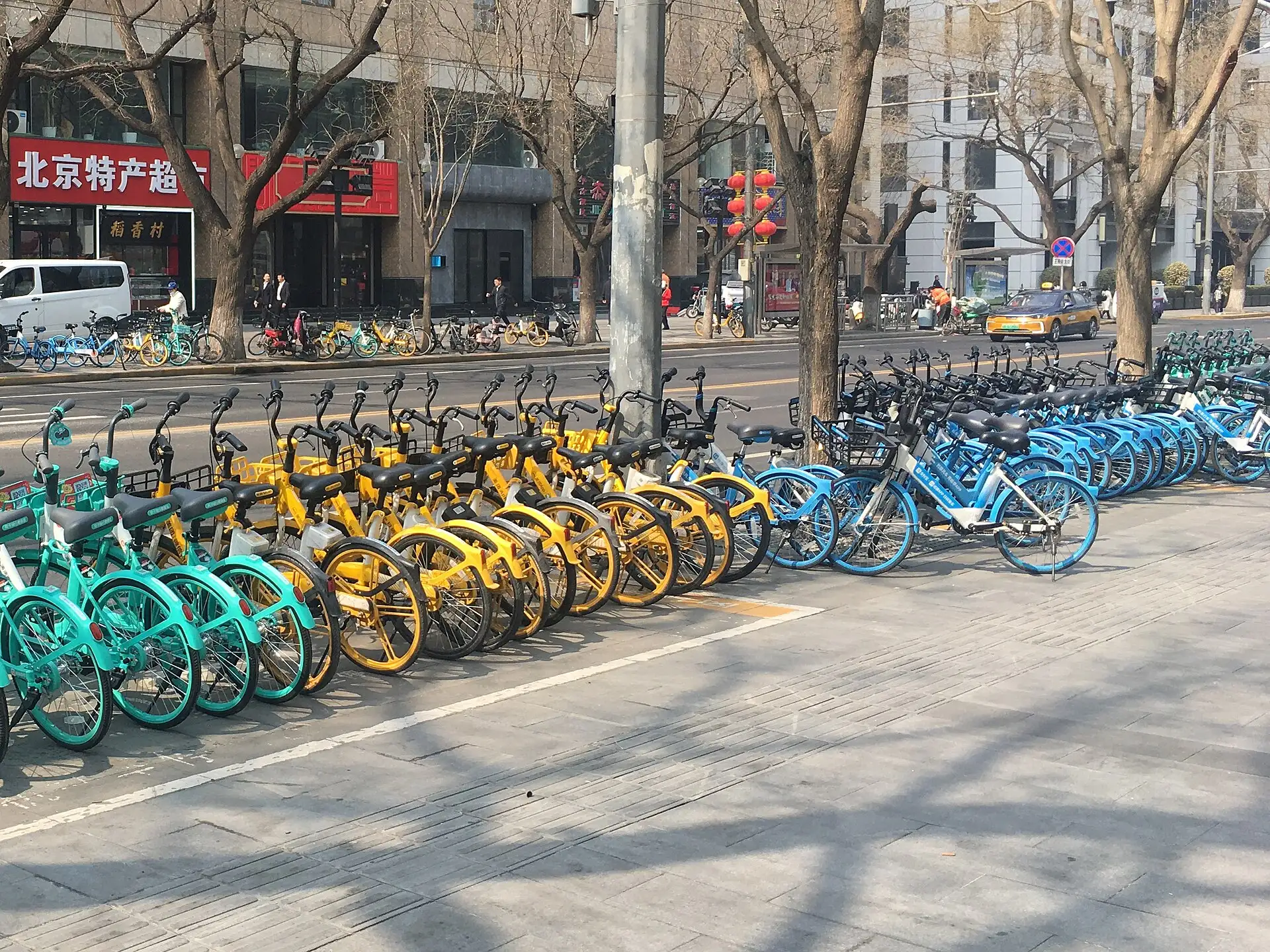 Reihe bunter Leihräder am Straßenrand in Peking, dahinter ein Laden mit chinesischem Schild